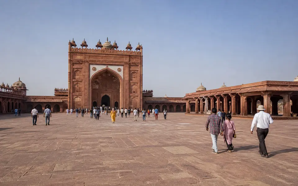 Wide view of Fatehpur Sikri’s red sandstone courtyards and gateways with scattered visitors walking in the open sun.