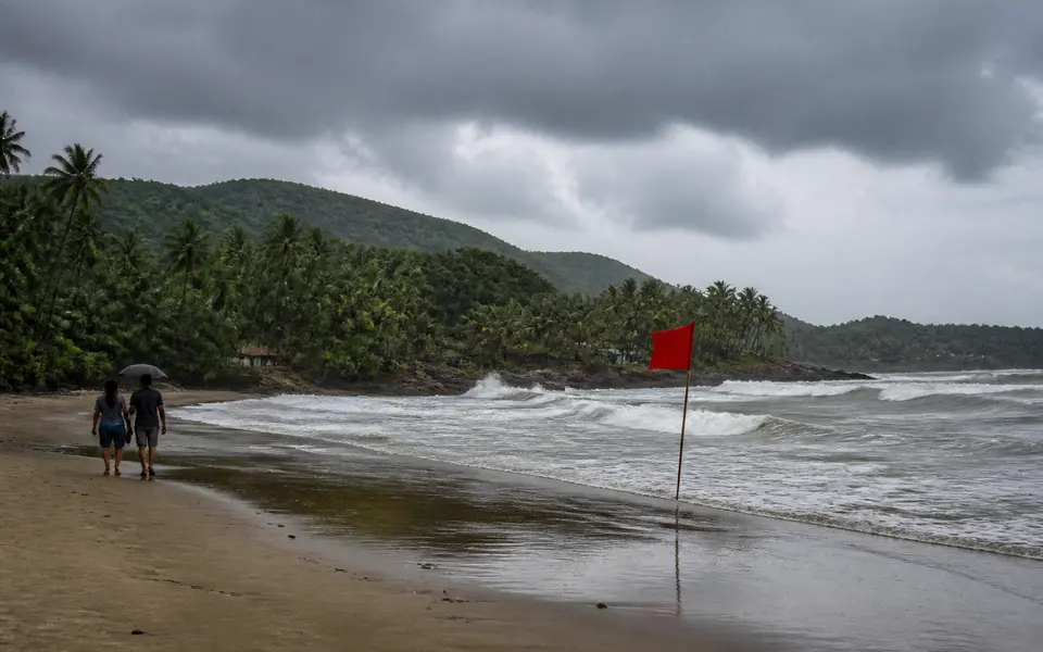 Goa beach in the monsoon with overcast skies, rough sea and green hills.