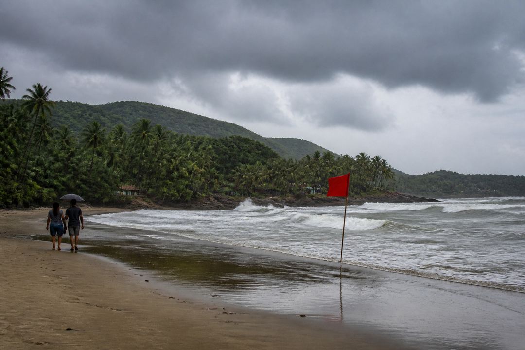 Goa beach in the monsoon with overcast skies, rough sea and green hills.