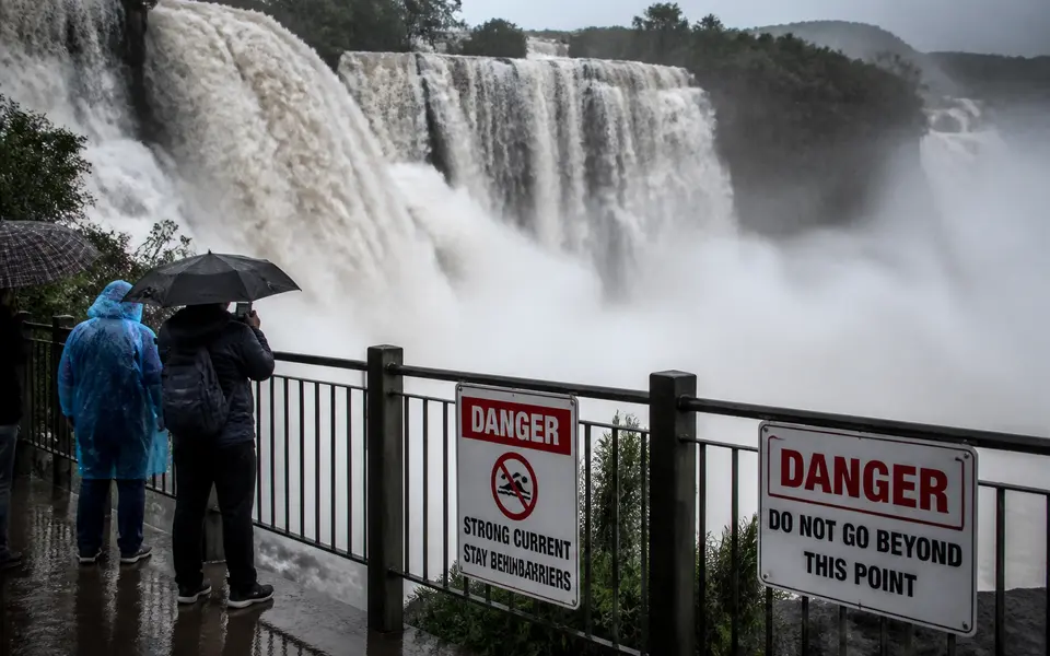 Indian waterfall in monsoon season with high water flow, safety barriers and warning signs, while visitors stand behind the railing.