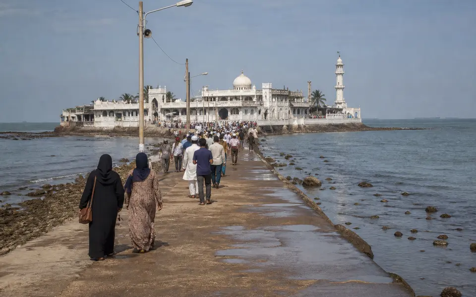 Haji Ali Dargah in Mumbai reached by a causeway, with visitors walking towards the white shrine at low tide.