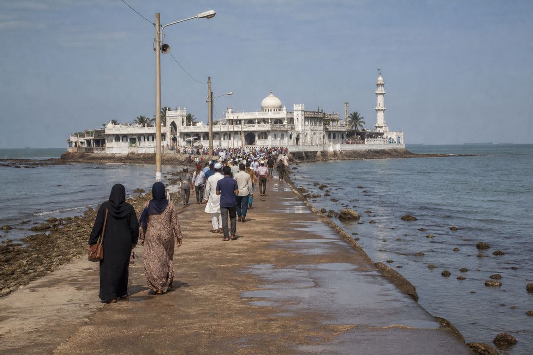 Haji Ali Dargah in Mumbai reached by a causeway, with visitors walking towards the white shrine at low tide.