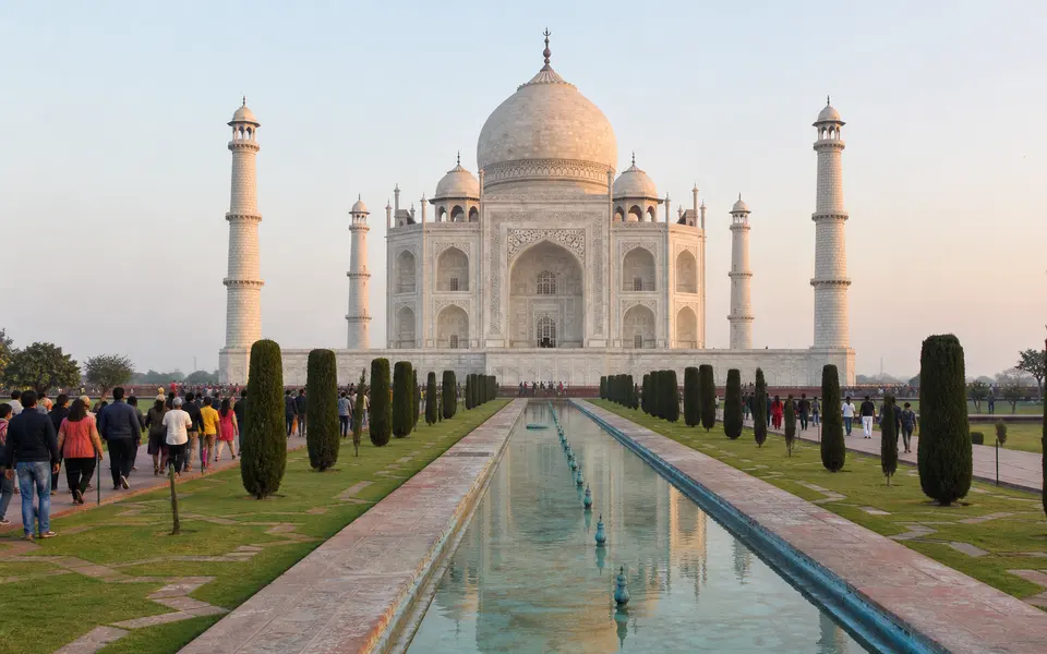 Taj Mahal in soft early-morning light with visitors walking along the main reflecting pool and moderate crowds.