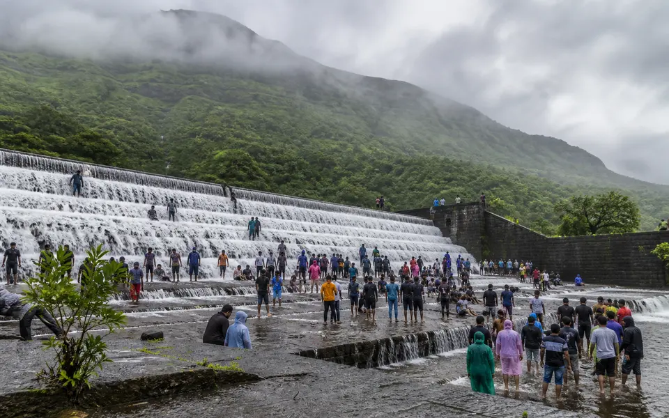 Monsoon water flowing over the steps of a dam near Lonavala with visitors standing at the edge and green hills behind.