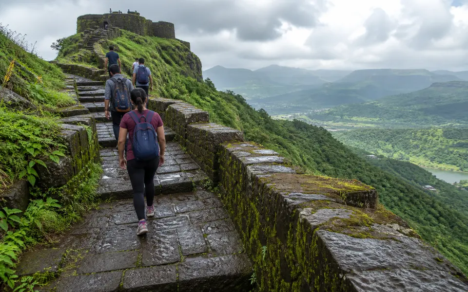 Walkers climbing stone steps towards a hill fort near Lonavala with valleys visible in the distance.