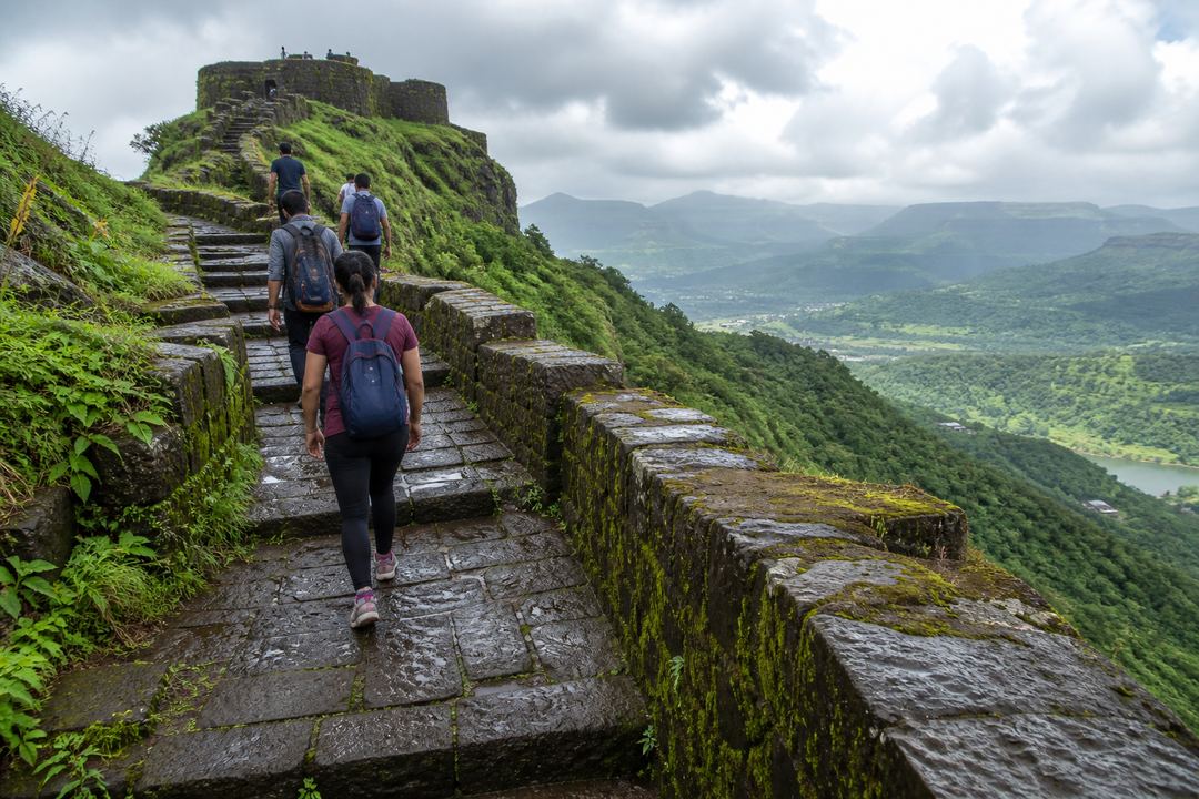 Walkers climbing stone steps towards a hill fort near Lonavala with valleys visible in the distance.