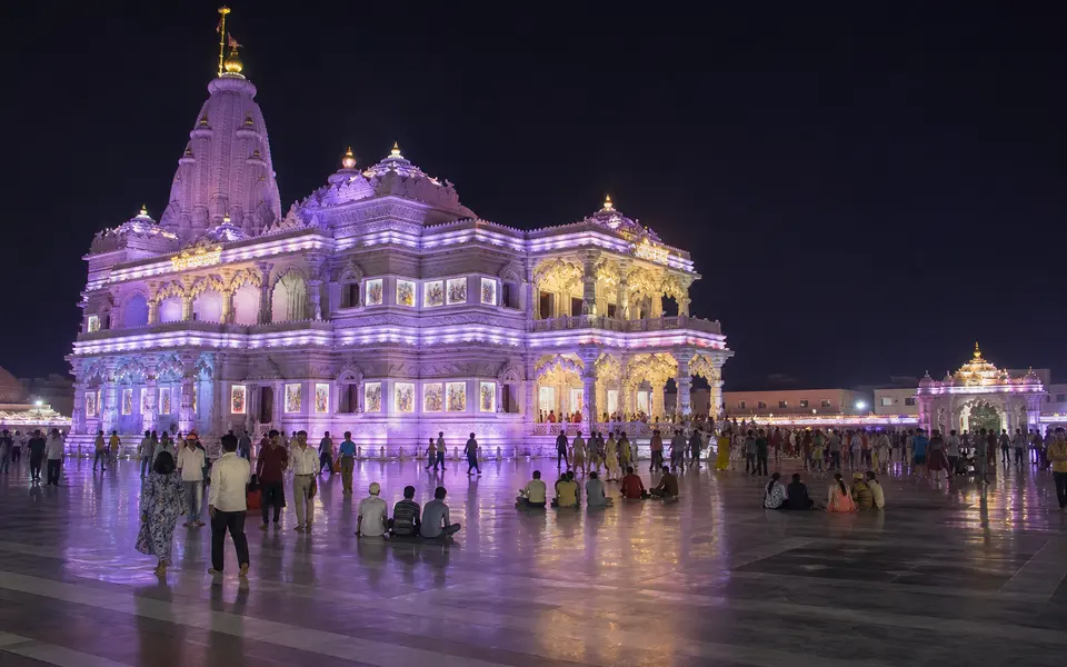 Night view of Prem Mandir in Vrindavan illuminated with colourful lights and devotees in the courtyard.