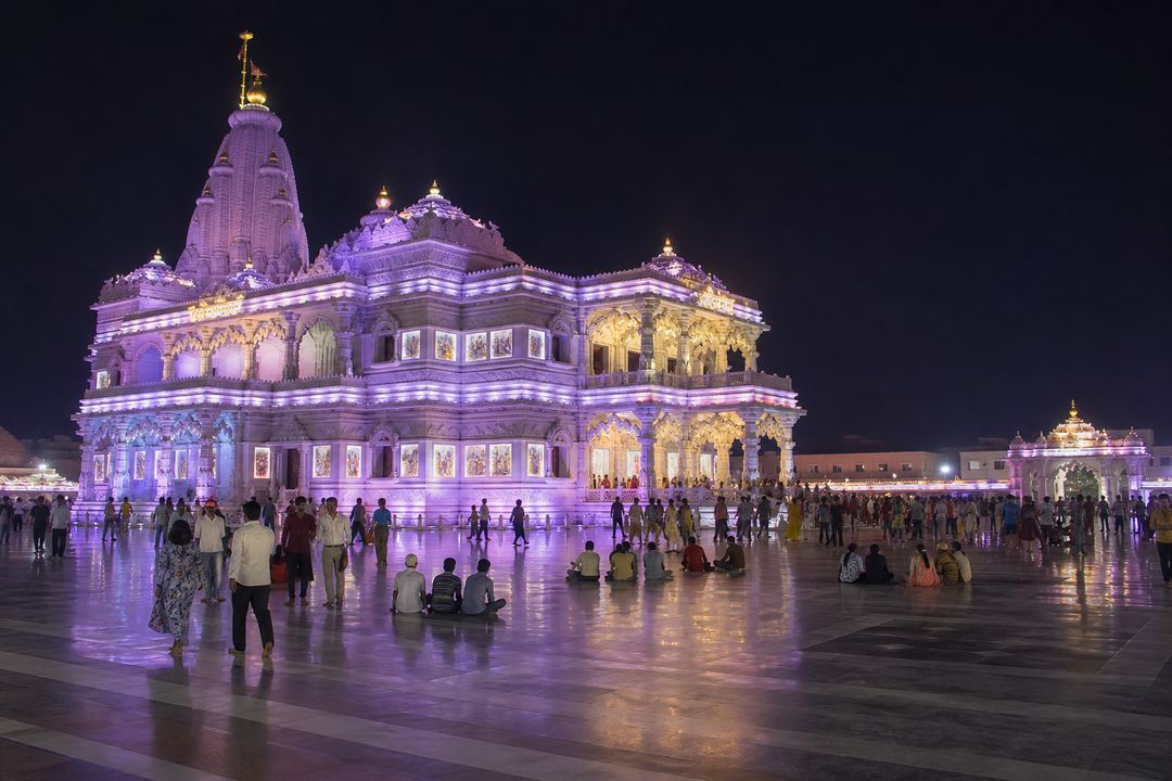 Night view of Prem Mandir in Vrindavan illuminated with colourful lights and devotees in the courtyard.