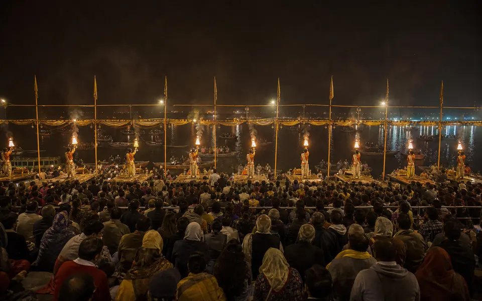 Evening Ganga Aarti at Dashashwamedh Ghat viewed from behind a large crowd with priests holding lamps near the river.
