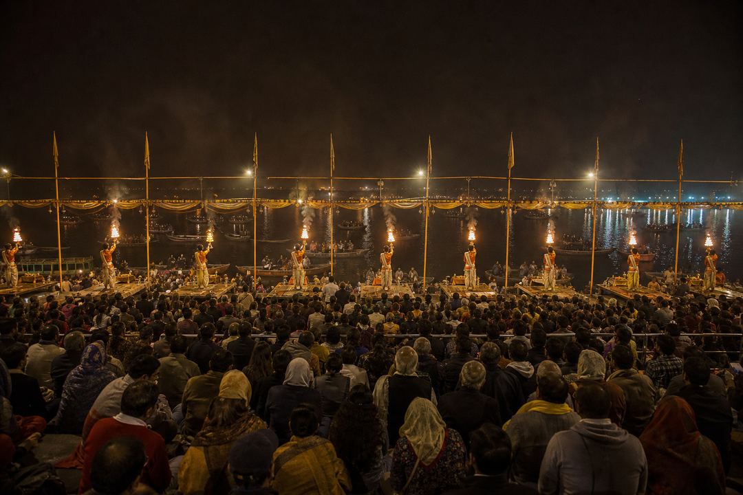 Evening Ganga Aarti at Dashashwamedh Ghat viewed from behind a large crowd with priests holding lamps near the river.