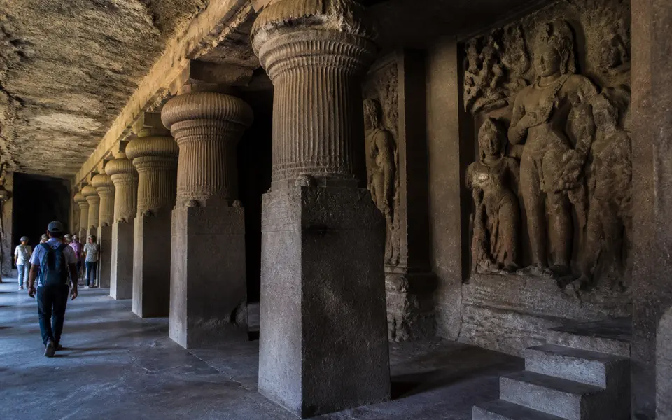 Stone sculptures inside Elephanta Caves near Mumbai with a visitor walking along the carved pillars.