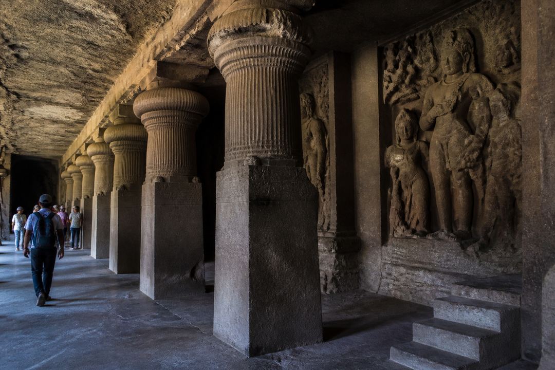 Stone sculptures inside Elephanta Caves near Mumbai with a visitor walking along the carved pillars.