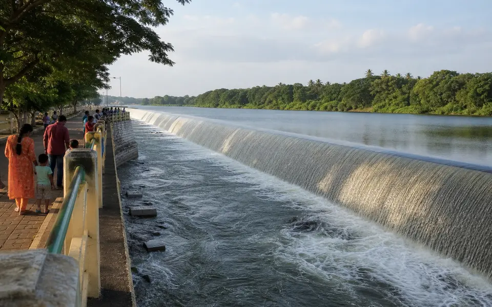 Families walking along a safe viewing area near Kallanai (Grand Anicut) dam on the Cauvery river, with water flowing over the stone structure.