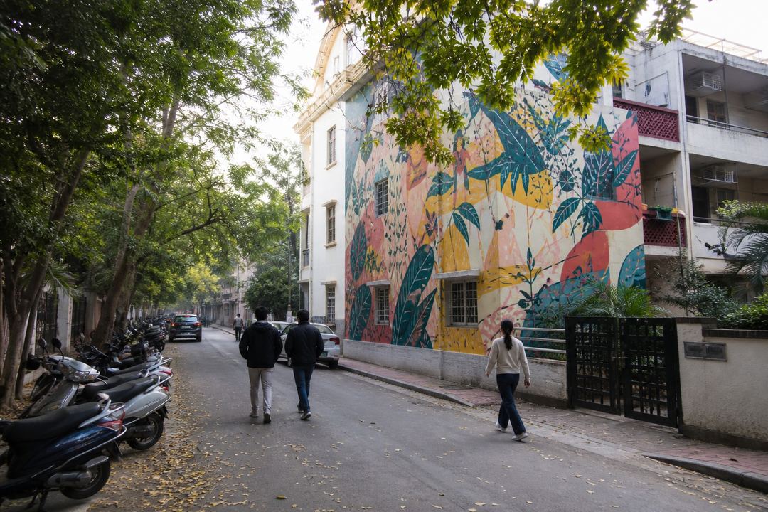 Colourful mural on a residential building in Lodhi Art District in Delhi, with a few walkers and parked scooters along a quiet street.