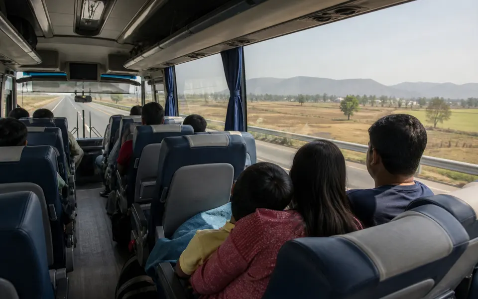 Interior of a modern air-conditioned intercity coach with an Indian family seated comfortably as the bus travels on a highway towards distant hills.