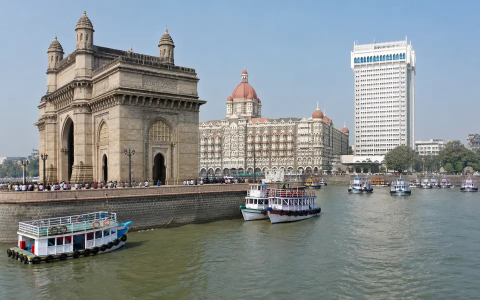 Gateway of India arch on Mumbai’s waterfront with boats in the harbour and heritage buildings behind it on a clear morning.