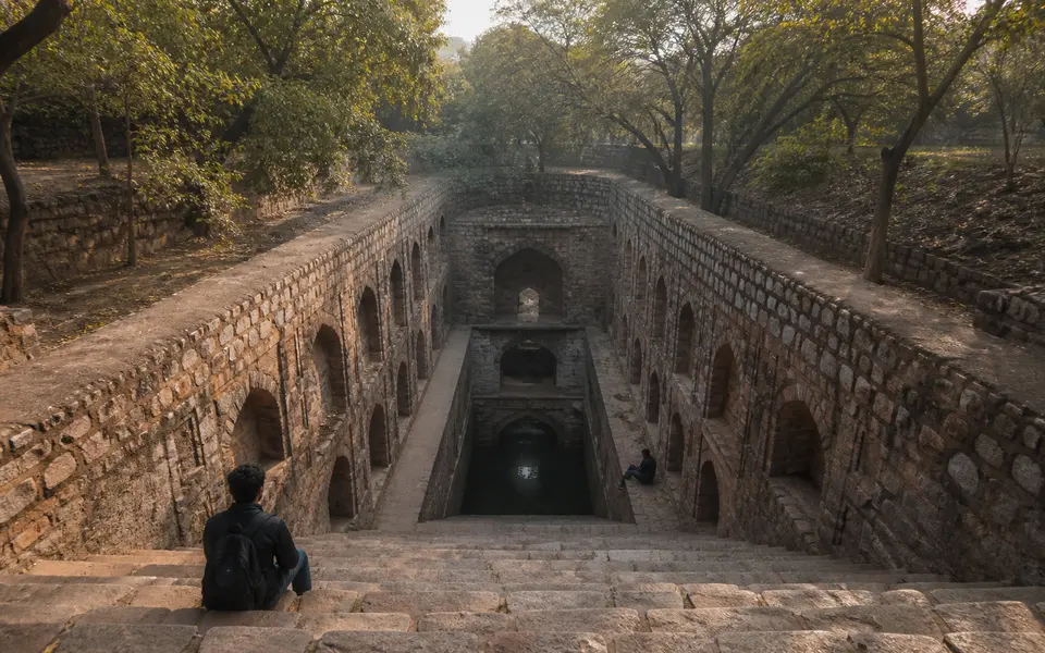 Quiet morning at Rajon ki Baoli stepwell in Mehrauli Archaeological Park in Delhi, with repeating stone arches and only one or two visitors in the frame.