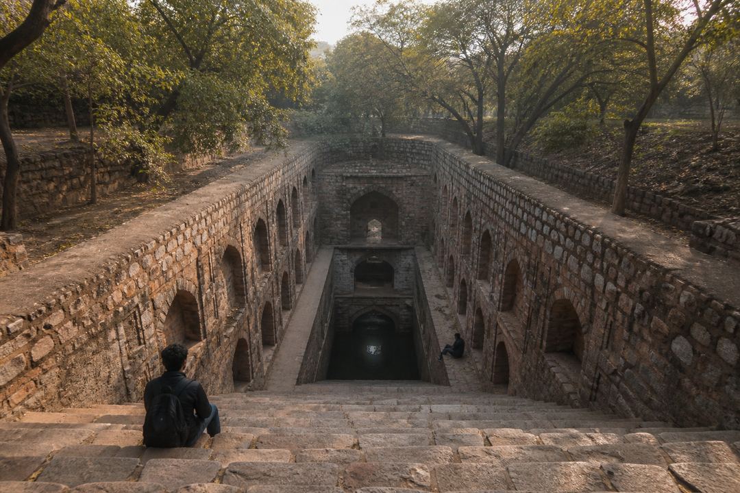 Quiet morning at Rajon ki Baoli stepwell in Mehrauli Archaeological Park in Delhi, with repeating stone arches and only one or two visitors in the frame.