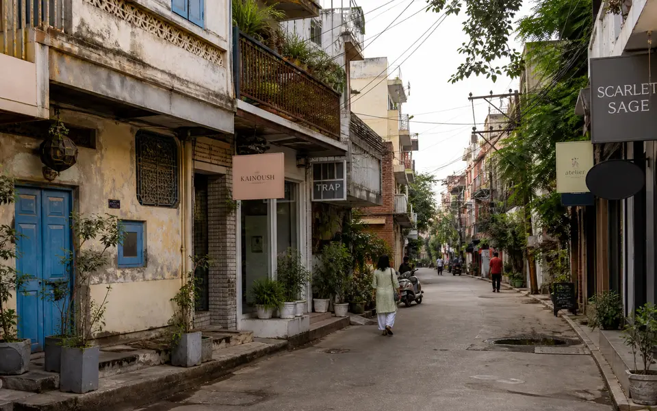 Narrow lane in Shahpur Jat village in Delhi with old houses, colourful boutique signboards and a few pedestrians on a calm weekday morning.