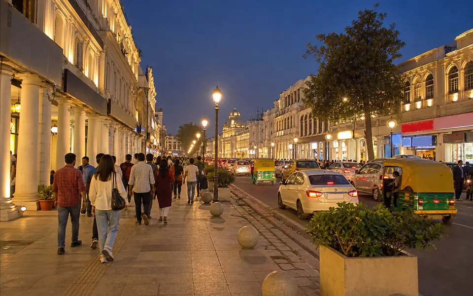 Evening view of Hazratganj in Lucknow with pedestrians, lit shopfronts and a line of cars along the road.
