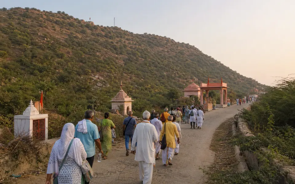 Pilgrims walking along the Govardhan parikrama path with Govardhan Hill and small roadside shrines in view during early morning light.