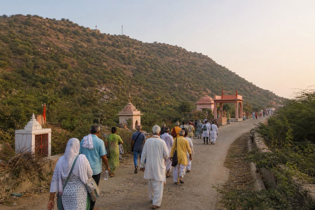 Pilgrims walking along the Govardhan parikrama path with Govardhan Hill and small roadside shrines in view during early morning light.