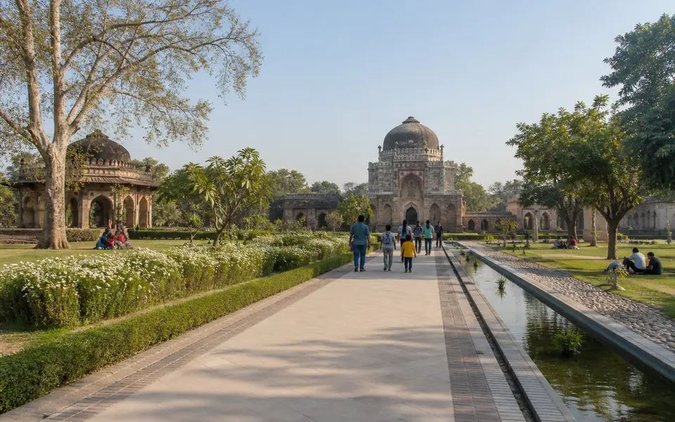 Wide path flanked by lawns, flower beds and heritage pavilions inside Sunder Nursery in Delhi, with a few families walking in soft morning light.