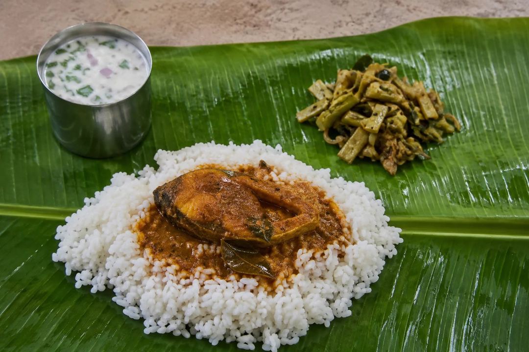 A cooked coastal Tamil fish curry served with rice a vegetable side and buttermilk on a banana leaf