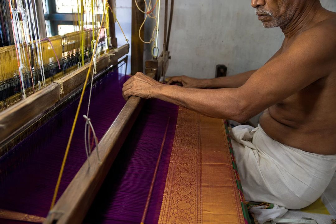 A handloom weaver working carefully on a richly coloured silk saree with a contrasting border