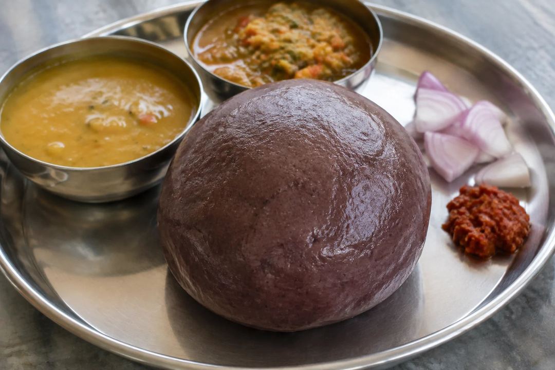 A smooth ball of ragi sangati served with lentil and vegetable gravies onion and chilli accompaniment