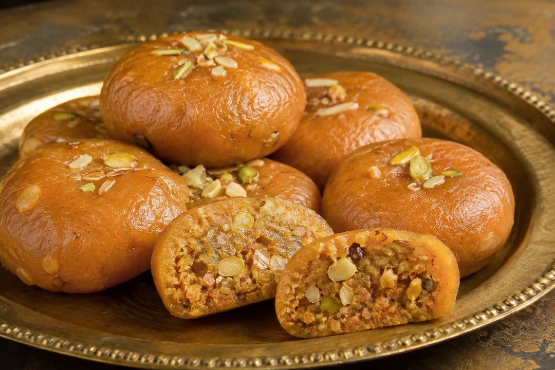 Golden brown Arcot style Makkan Peda sweets with one cut open to show the nutty filling