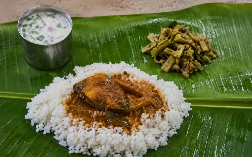 A cooked coastal Tamil fish curry served with rice a vegetable side and buttermilk on a banana leaf