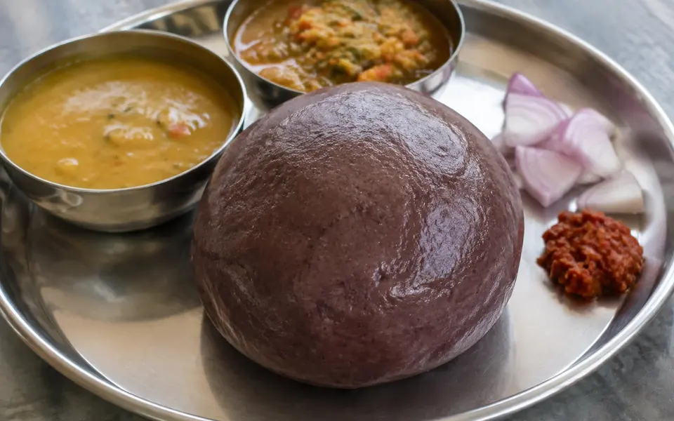A smooth ball of ragi sangati served with lentil and vegetable gravies onion and chilli accompaniment