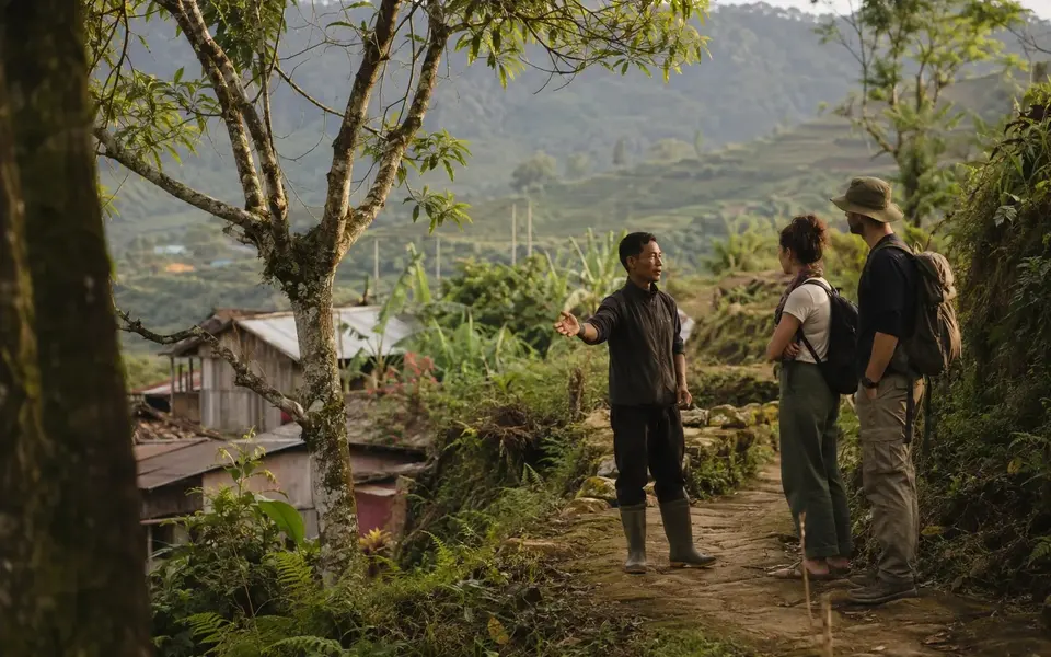 A local guide explains forest and village stewardship to two visitors in Northeast India.
