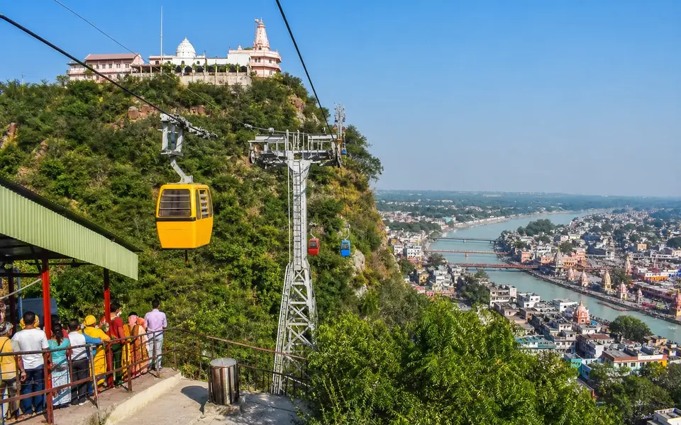 Ropeway cabins heading up to a hilltop temple above Haridwar with the city and Ganga visible below.