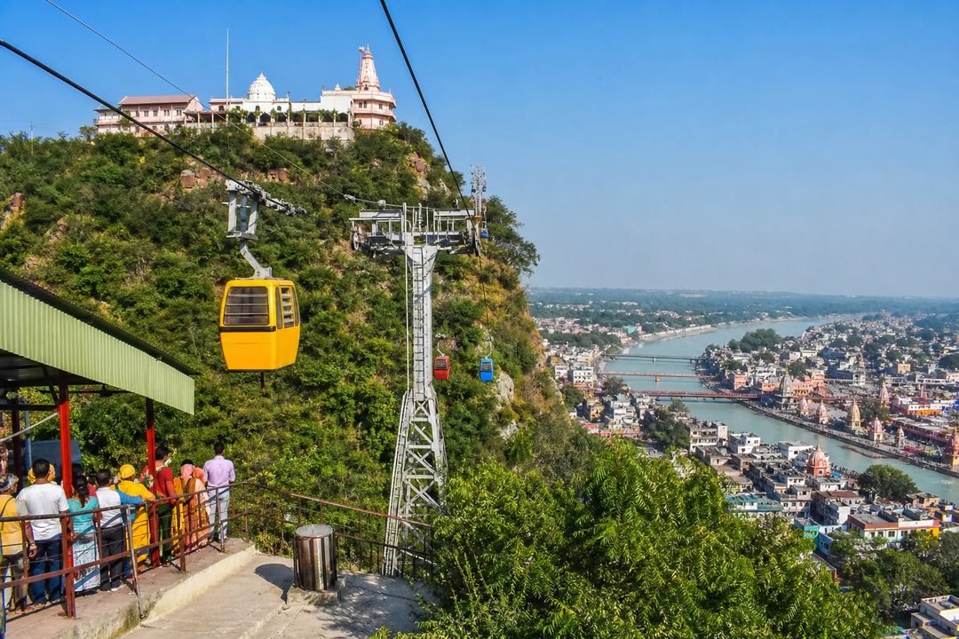 Ropeway cabins heading up to a hilltop temple above Haridwar with the city and Ganga visible below.
