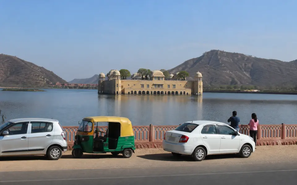 Roadside view of Jal Mahal in Jaipur, with the palace sitting in the middle of the lake and cars briefly stopped along the lakeside road.