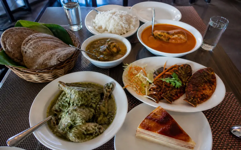Casual Goan meal spread with fish curry, rice, fried fish, poi bread and bebinca dessert on a table in a simple restaurant.