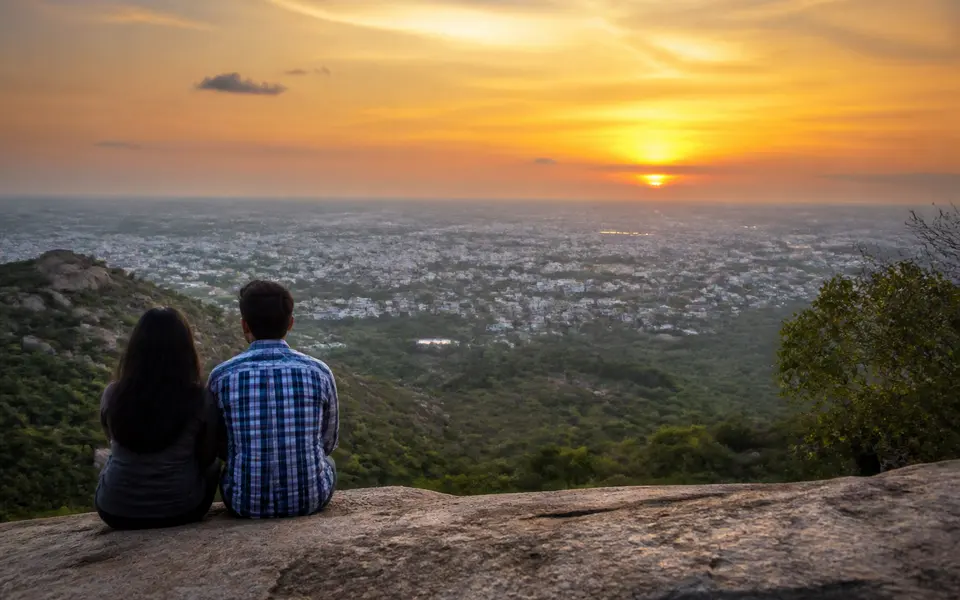Couple sitting on a rock at Samanar Hills overlooking Madurai at sunset, with warm light and open sky.