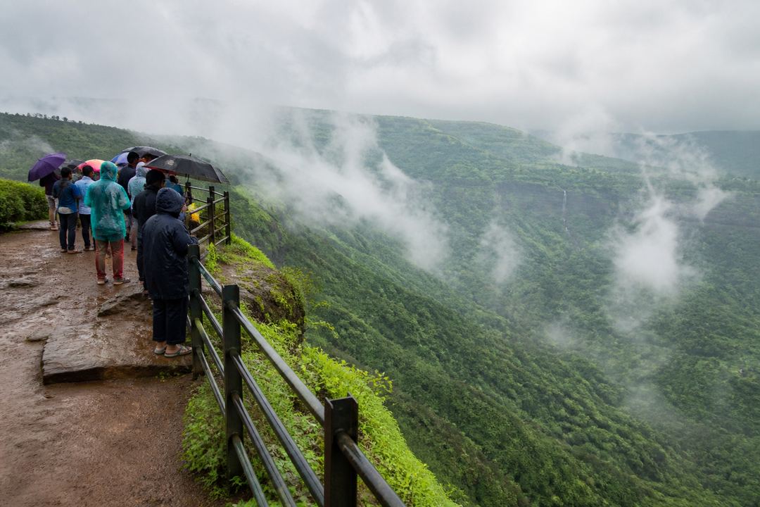 Clifftop viewpoint near Lonavala with green Western Ghats valleys and low monsoon clouds.