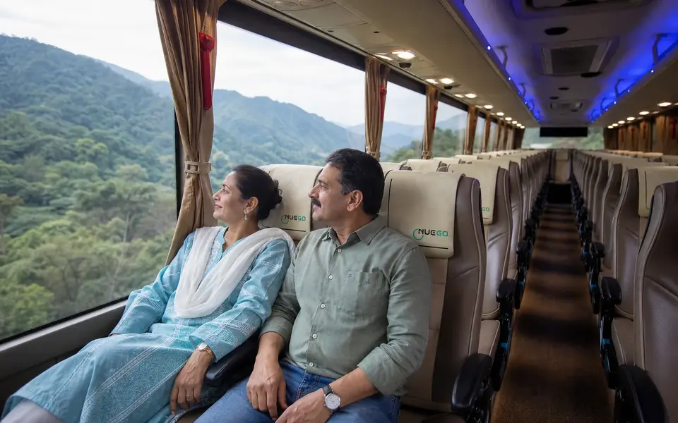 Couple seated together inside a NueGo electric intercity coach on the Delhi–Rishikesh route, looking towards the hills.