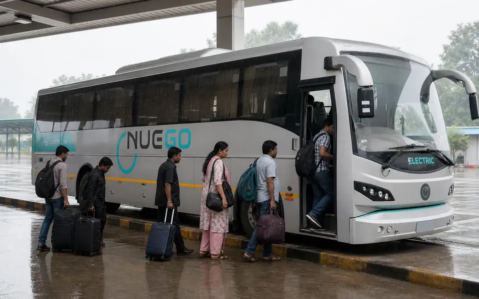 Travellers boarding a NueGo electric intercity coach at a covered bus bay during light monsoon rain in India.