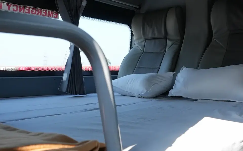 Interior view of a NueGo sleeper berth with mattress, pillows, privacy curtain, ventilation outlets and safety rail.