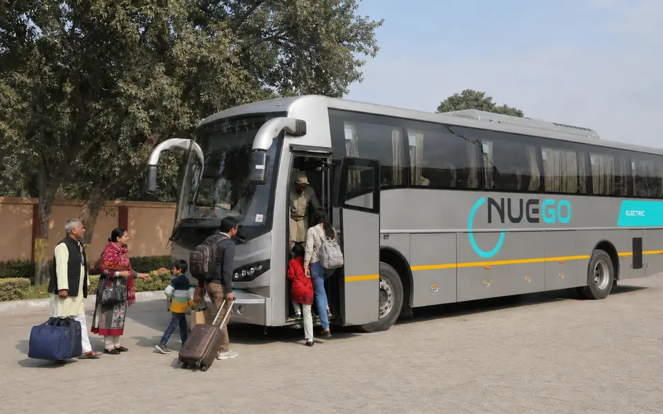 Clearly branded NueGo electric intercity coach travelling on an Indian highway, photographed from outside.