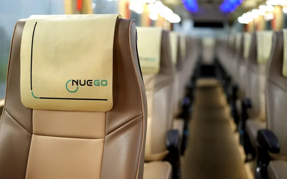 Close view of a NueGo reclining coach seat with branded headrest cover and other seats aligned behind it.