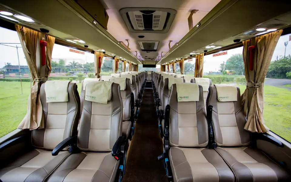 Wide view down the aisle of a clean NueGo intercity coach with reclining seats, overhead lighting and marked emergency exits.
