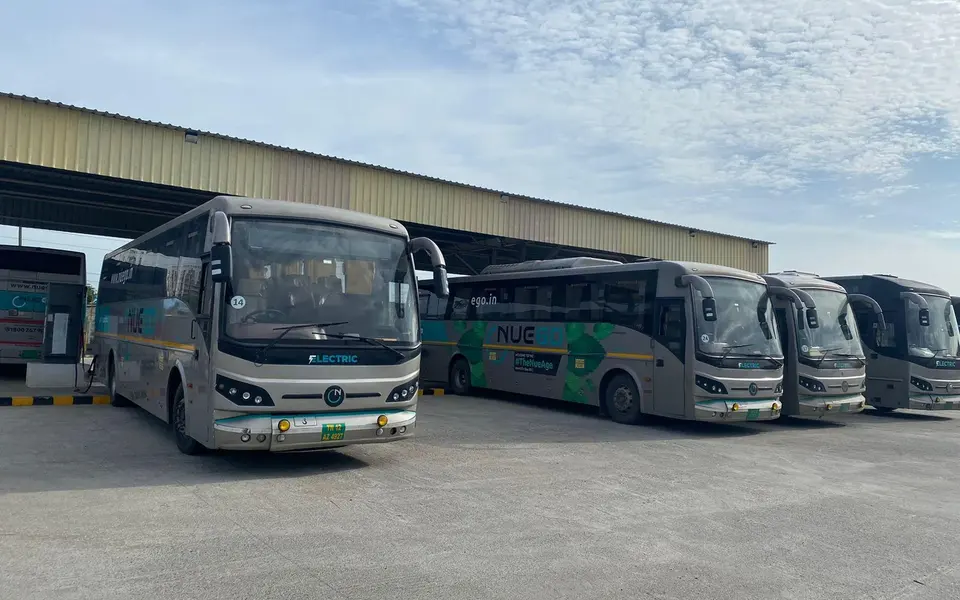 Several silver and teal NueGo electric intercity coaches parked in a depot under a blue sky.