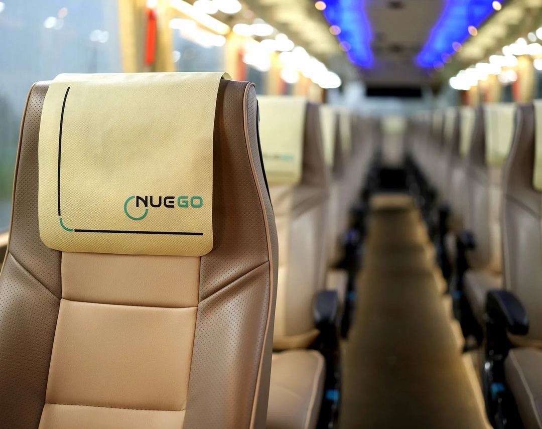 Close view of a comfortable NueGo-branded coach seat with the softly lit passenger cabin visible behind it.