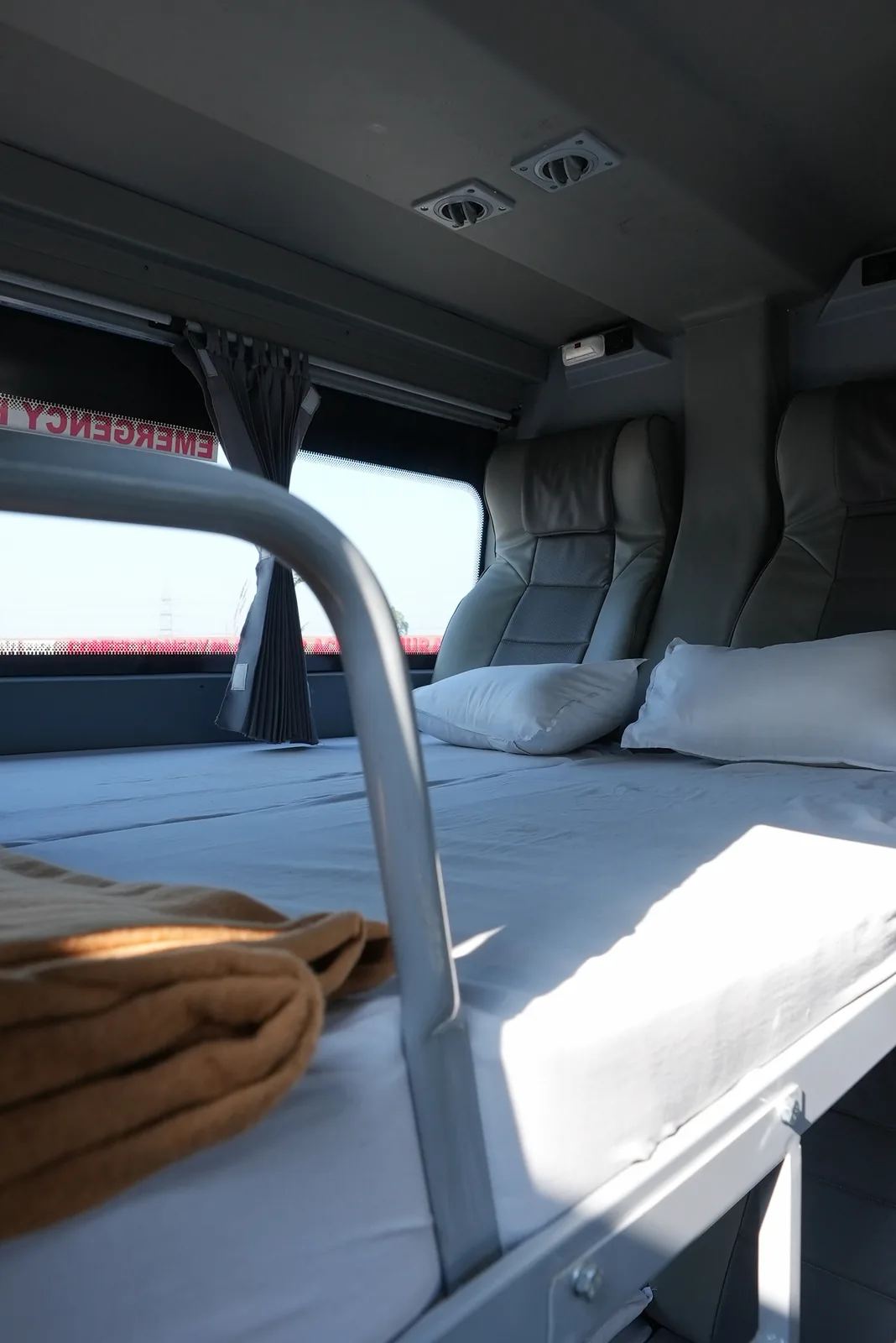 A clean NueGo sleeper coach berth with pillows, curtains and a reading light.