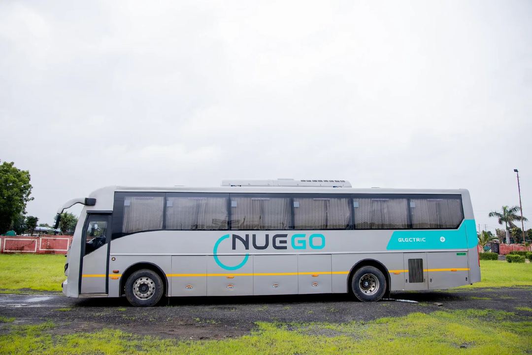 Full side profile of a silver and teal NueGo electric intercity coach parked beside a green verge.